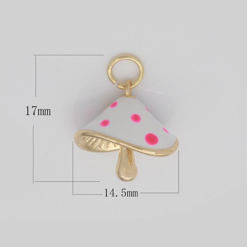 May include: Gold-tone mushroom charm with a white enamel finish and pink polka dots. The charm measures 17 mm in height and 14.5 mm in width.