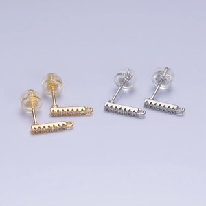 May include: Two pairs of earring findings with a clear plastic post and a silver or gold bar with a small loop at the end. The bar is decorated with small clear rhinestones.