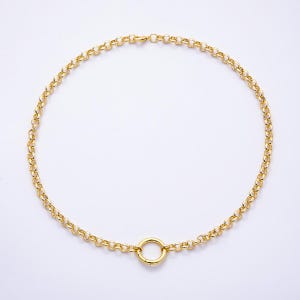 May include: A gold-toned chain necklace featuring a series of uniform circular links connected in a continuous loop. The necklace includes a larger, singular circular ring positioned at the bottom center, serving as a focal point for the design.