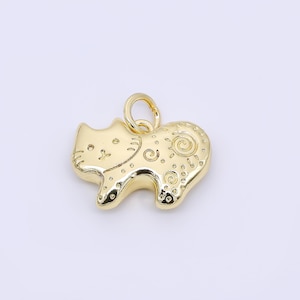 May include: A gold-colored cat-shaped pendant with a loop for hanging. The pendant features etched details on the body and face, including swirls and dots. The cat is in a standing position.