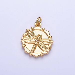 May include: A gold-toned pendant featuring a detailed dragonfly design with a clear rhinestone in the center. The dragonfly is surrounded by a circular, octagonal frame with a textured surface.