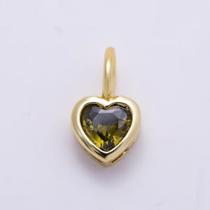 May include: A heart-shaped pendant featuring a faceted olive green gemstone set within a polished gold-toned metal frame. The pendant includes a small, smooth gold-toned bail at the top for attachment to a chain or necklace, showcasing a classic design.
