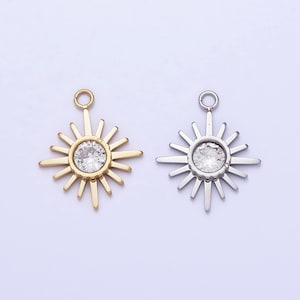 Puede incluir: Dos colgantes de sol con un centro de cristal de roca transparente. El colgante de la izquierda es dorado y el de la derecha es plateado.