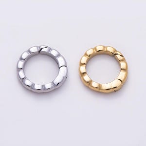 May include: Two circular spring gate rings, one in a polished silver tone and one in a polished gold tone. Each ring features a segmented, scalloped outer edge and a functional spring-loaded opening mechanism for attaching items securely.