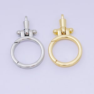 Pode incluir: São apresentados dois fechos giratórios de metal, um prateado e outro dourado. Cada fecho apresenta um anel circular com uma abertura articulada e um topo decorativo com pequenos detalhes de bola. Estes fechos são para malas ou acessórios.