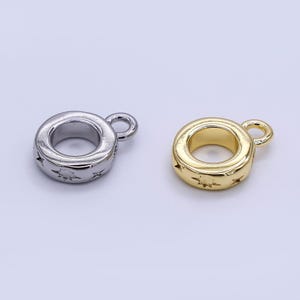 May include: Two metal charm beads, one silver and one gold, each with a circular design and a small loop. The beads have star cutouts around the sides. These charms are suitable for jewelry making.