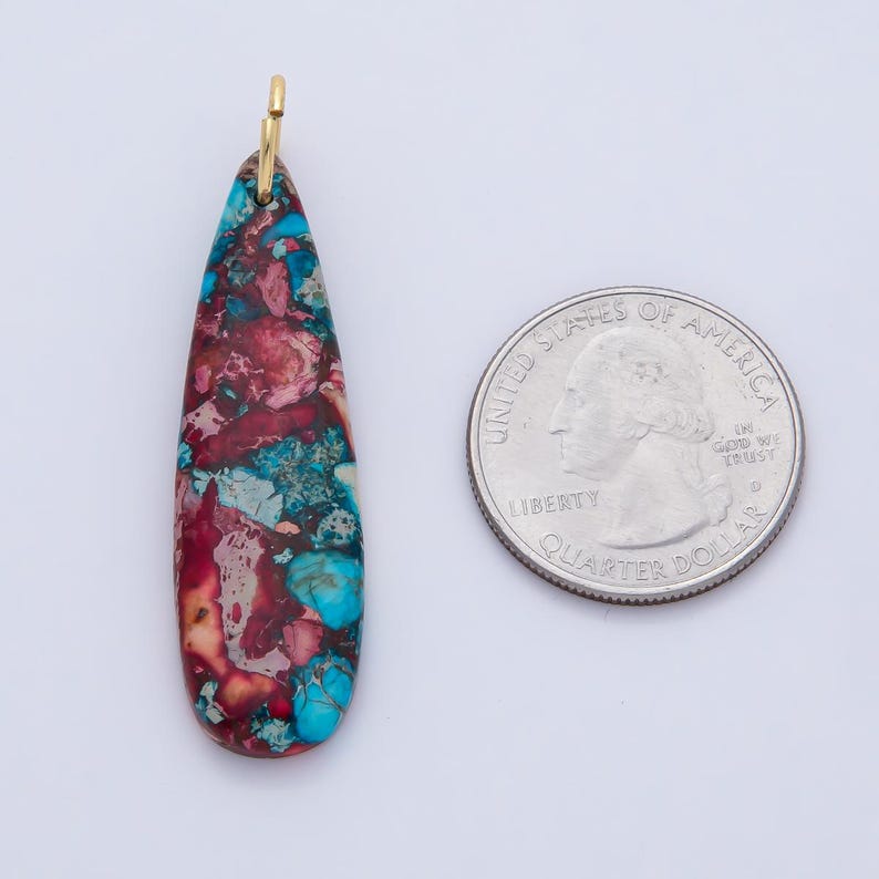 May include: A teardrop-shaped pendant with a gold-colored bail. The pendant features a mosaic pattern of red, blue, and cream-colored stone. A U.S. quarter is next to the pendant for size comparison.