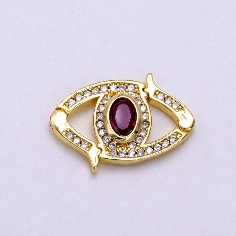 May include: Gold-tone eye charm with a red gemstone and clear crystal accents.