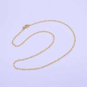May include: A gold chain necklace with a lobster clasp closure. The chain is made of small, linked, rectangular shapes.