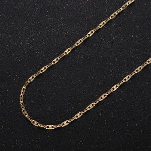 May include: A gold chain necklace with a delicate, intricate design. The chain is made of small, linked pieces that create a subtle pattern.