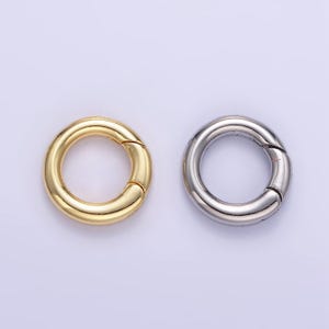 Könnte beinhalten: Zwei Metallringe, einer golden und einer silbern, mit einem geteilten Ringdesign. Die Ringe haben einen Durchmesser von etwa 2,5 cm.