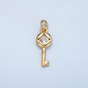 Puede incluir: Un dije de llave de oro con un strass transparente en el centro. La llave tiene una cabeza redonda y un diseño simple.