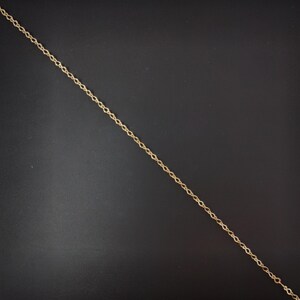 Op de afbeelding: Een gouden ketting met een delicaat, gedraaid ontwerp. De ketting ligt plat op een zwart oppervlak.