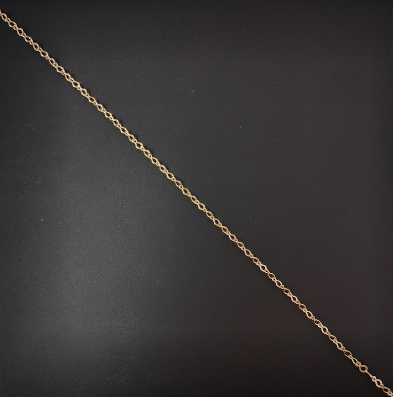 Op de afbeelding: Een gouden ketting met een delicaat, gedraaid ontwerp. De ketting ligt plat op een zwart oppervlak.