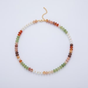 May include: A colorful beaded necklace featuring a variety of earth-toned beads, including white, orange, green, and brown. The necklace has a gold-colored chain and clasp. The beads are small and round, creating a delicate and elegant look.