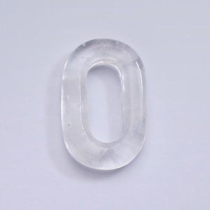May include: A clear crystal charm shaped like the number zero. The charm is smooth and polished.