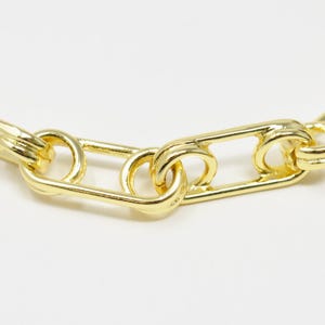 May include: Close-up of a gold chain necklace with a safety pin link design.