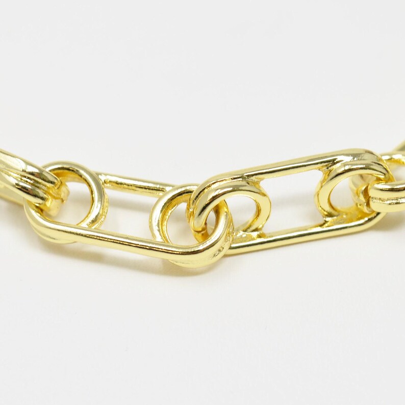 May include: Close-up of a gold chain necklace with a safety pin link design.