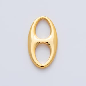 May include: A gold-coloured pendant with an elongated oval shape and a central opening. The smooth, reflective surface catches the light, highlighting its glossy finish. The design is simple yet elegant, suitable for various jewellery applications.