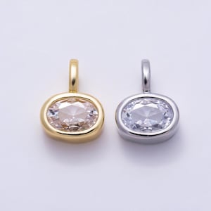 May include: Two oval-shaped pendants featuring faceted clear stones set in metal. One pendant has a polished gold-tone finish, while the other has a polished silver-tone finish. Each piece includes a small vertical loop at the top for attachment.