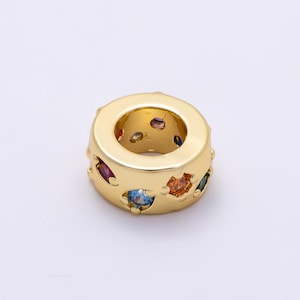 May include: A gold-toned cylindrical bead featuring a smooth, polished surface with multiple star-shaped cutouts. Each cutout is set with a small, round, multi-colored gemstone, including red, blue, orange, and green stones embedded in the metal.