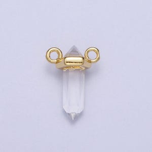 May include: Gold-toned crystal point charm with two jump rings. The crystal is clear and faceted.
