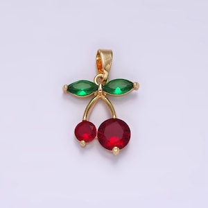 May include: A gold-colored pendant in the shape of cherries. The pendant features two round, red gemstones representing the cherries, and two green, marquise-cut gemstones for the leaves. The pendant is designed with a loop for a chain.