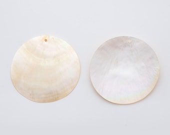 May include: Two round, iridescent mother-of-pearl shell pendants. The pendants are a creamy white color with a natural, swirling pattern. Each pendant has a small hole at the top for stringing. These pendants are ideal for jewelry making.