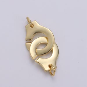 May include: Gold-toned metal charm in the shape of handcuffs. The charm is designed to be attached to a necklace or bracelet.