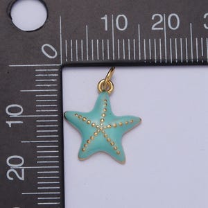 May include: A turquoise starfish charm with gold-colored accents. The five-pointed star has a gold-colored border and small gold dots. The charm has a small gold loop at the top for attaching to a necklace or bracelet. Jewelry accessory.