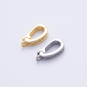 May include: Two metal jewelry clasps. One is gold-toned, the other is silver-toned. Both clasps have a curved, oval shape with a row of small, clear stones along the outer edge. Each clasp has a small loop at one end.