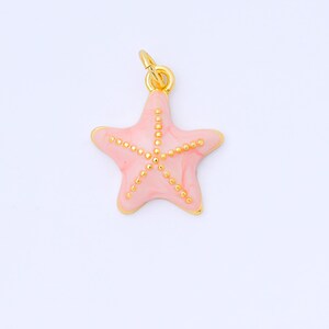 May include: A pink starfish charm with gold-colored accents. The charm has a gold-colored bail for attaching to a necklace or bracelet. The starfish is a light pink color with gold-colored dots.