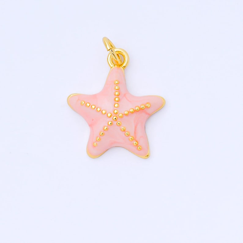 May include: A pink starfish charm with gold-colored accents. The charm has a gold-colored bail for attaching to a necklace or bracelet. The starfish is a light pink color with gold-colored dots.