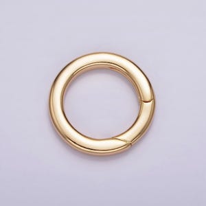 Pode incluir: Um anel de metal dourado com uma superf&iacute;cie lisa e arredondada. O anel &eacute; aberto de um lado, criando um la&ccedil;o.