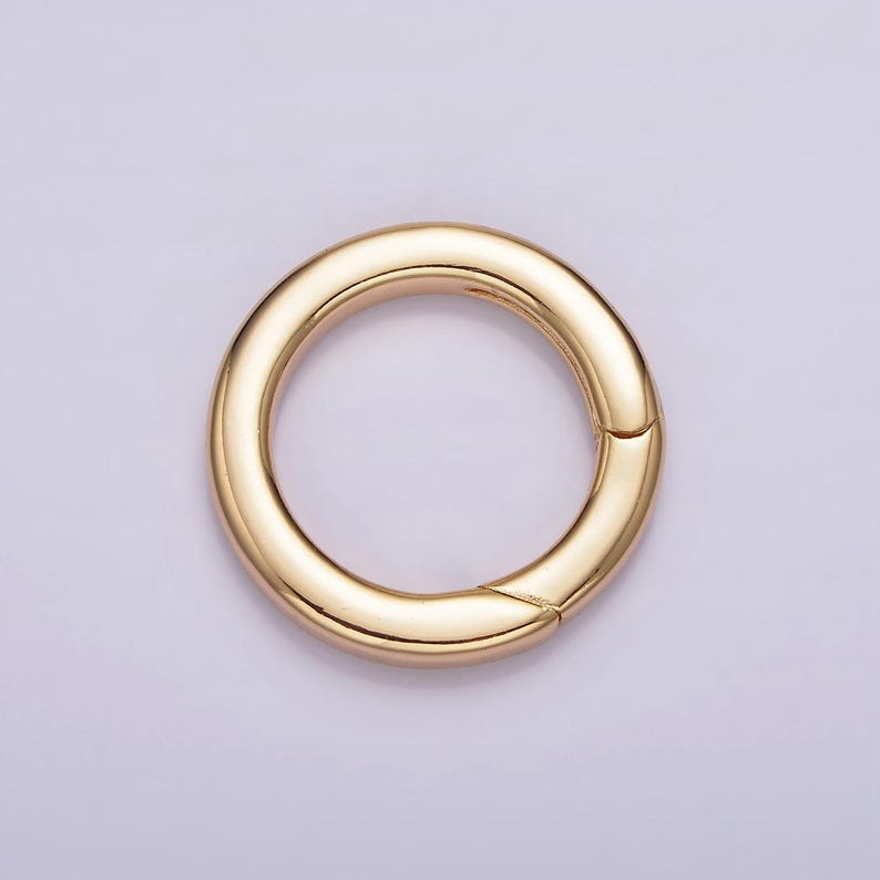 Pode incluir: Um anel de metal dourado com uma superf&iacute;cie lisa e arredondada. O anel &eacute; aberto de um lado, criando um la&ccedil;o.