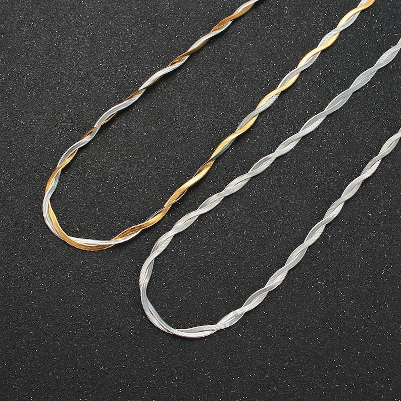 May include: Two twisted chain necklaces, one silver and one gold, on a black background.