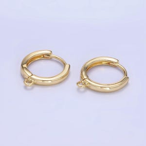 May include: Two gold-colored hoop earrings. Each earring has a rounded shape with a small loop at the bottom. The earrings are made of a shiny, metallic material and are set against a light background.