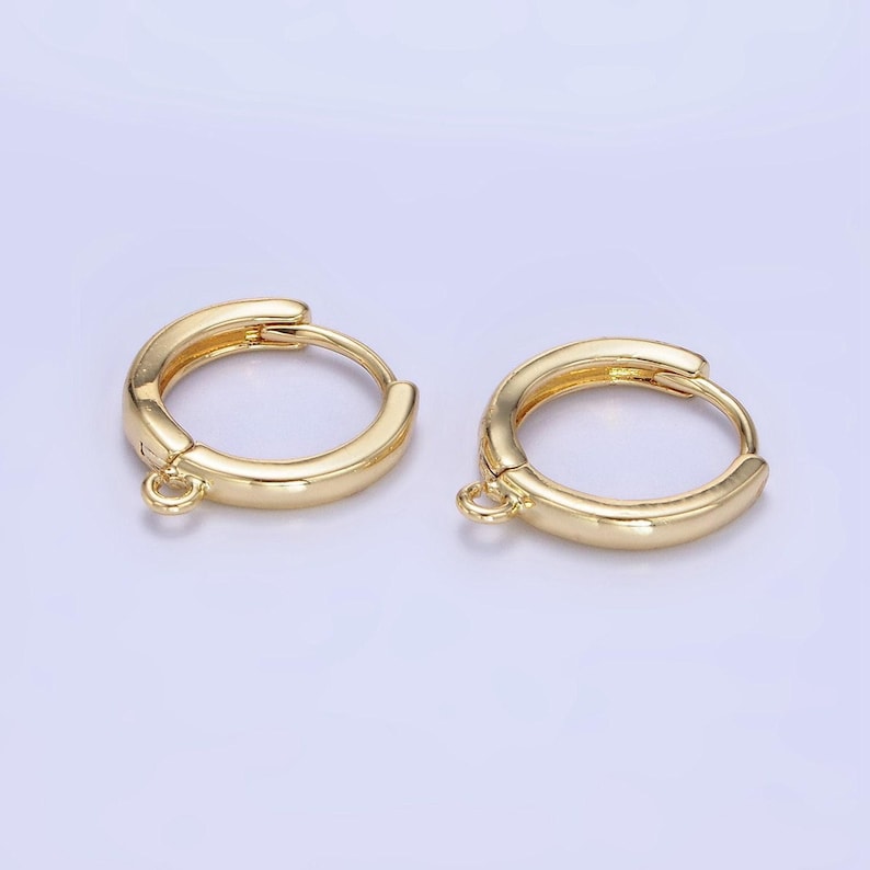 May include: Two gold-coloured hoop earrings. Each earring has a rounded shape with a small loop at the bottom. The earrings are made of a shiny, metallic material and are set against a light background.