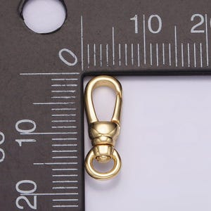 May include: Gold-toned metal clasp with a spring-loaded gate and a round ring. The clasp is about 1 inch long and is shown next to a ruler.