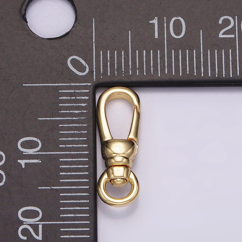 May include: Gold-toned metal clasp with a spring-loaded gate and a round ring. The clasp is about 1 inch long and is shown next to a ruler.
