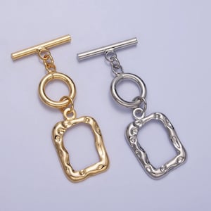 Op de afbeelding: Twee gouden en zilveren toggle-sluitingen met een ketting en een getextureerd rechthoekig frame. De sluitingen zijn perfect voor het maken van sieraden of om een ​​unieke touch toe te voegen aan tassen en andere accessoires.