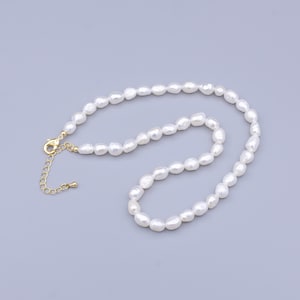 Könnte beinhalten: Eine weiße Perlenkette mit einem goldenen Verschluss und einer Verlängerungskette. Die Perlen sind unregelmäßig geformt und haben einen dezenten Glanz.