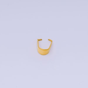 May include: A gold-colored, U-shaped metal object with a rounded base and two straight, open ends. The object has a smooth, reflective surface and is set against a plain white background. It appears to be a small, decorative item.
