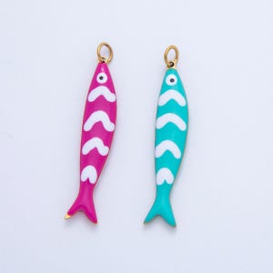 Peut inclure: Deux pendentifs en forme de poisson. L'un est magenta avec des chevrons blancs, l'autre est turquoise avec des chevrons blancs. Les deux ont des boucles dorées en haut pour être suspendus. Les pendentifs ont une queue de poisson.