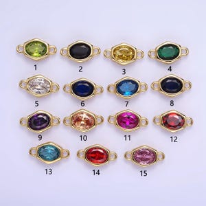 May include: Fifteen gold-tone connector charms with different colored oval-shaped gemstones. The charms have two loops on either side for attaching to jewelry.