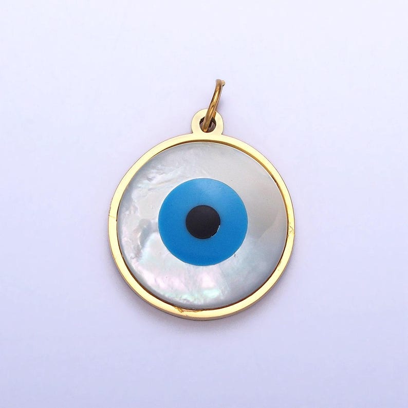 May include: Gold-toned pendant with a blue and black evil eye design on a white mother-of-pearl background.