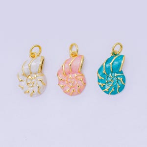 May include: Three seashell pendants in white, pink, and teal, each with gold-colored accents. The pendants have a spiral design and a loop for attaching to a chain or bracelet. The background is a solid, light color.