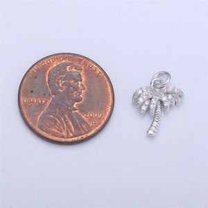 May include: Silver palm tree charm with clear cubic zirconia stones. The charm is about the size of a US penny.