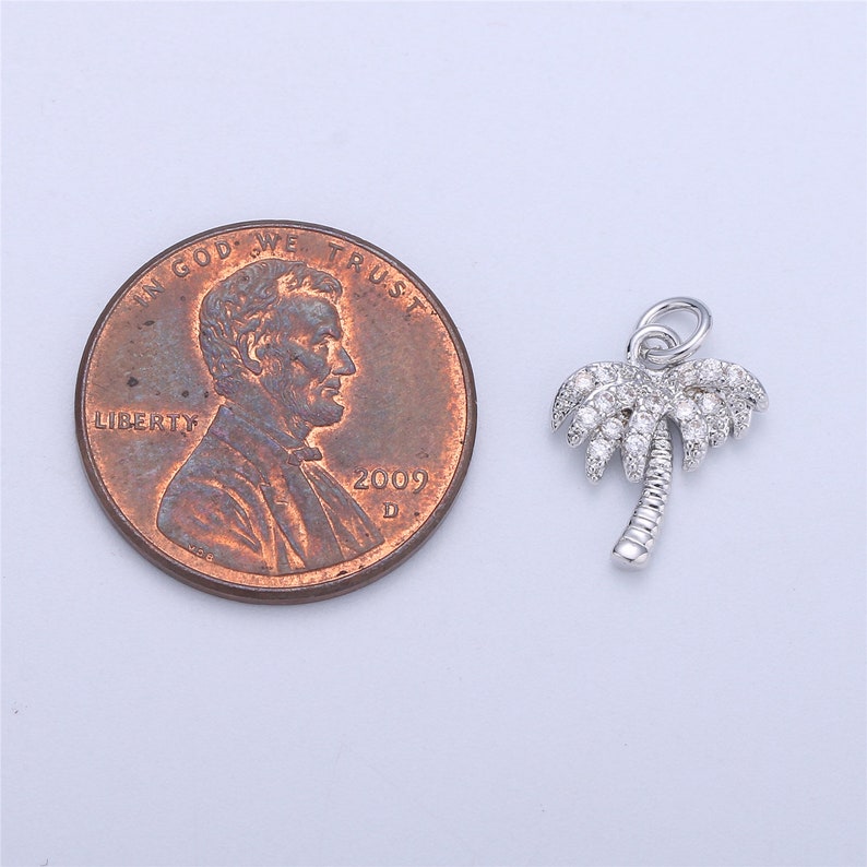 May include: Silver palm tree charm with clear cubic zirconia stones. The charm is about the size of a US penny.