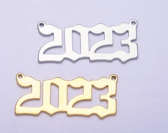 Könnte beinhalten: Zwei Metall-Anhänger in Form der Zahl 2023. Der obere Anhänger ist silberfarben und der untere Anhänger ist golden.